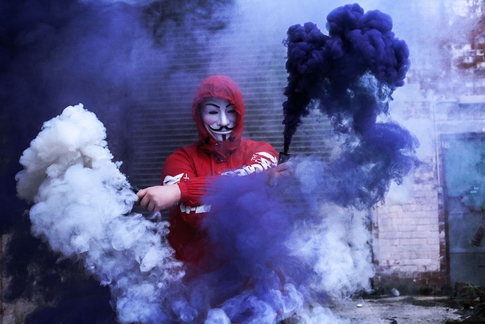 Hombre con sudadera con capucha roja de pie cerca de la pared gris durante la foto diurna