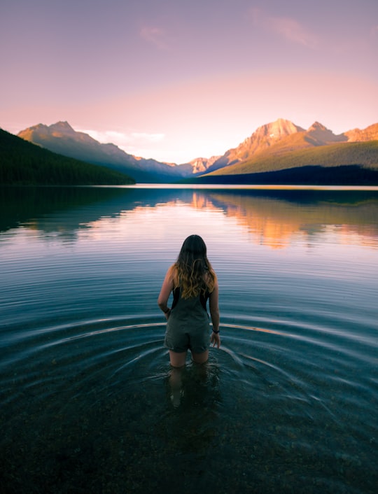 woman in blue overall shorts on body of water in Glacier National Park, Bowman Lake United States