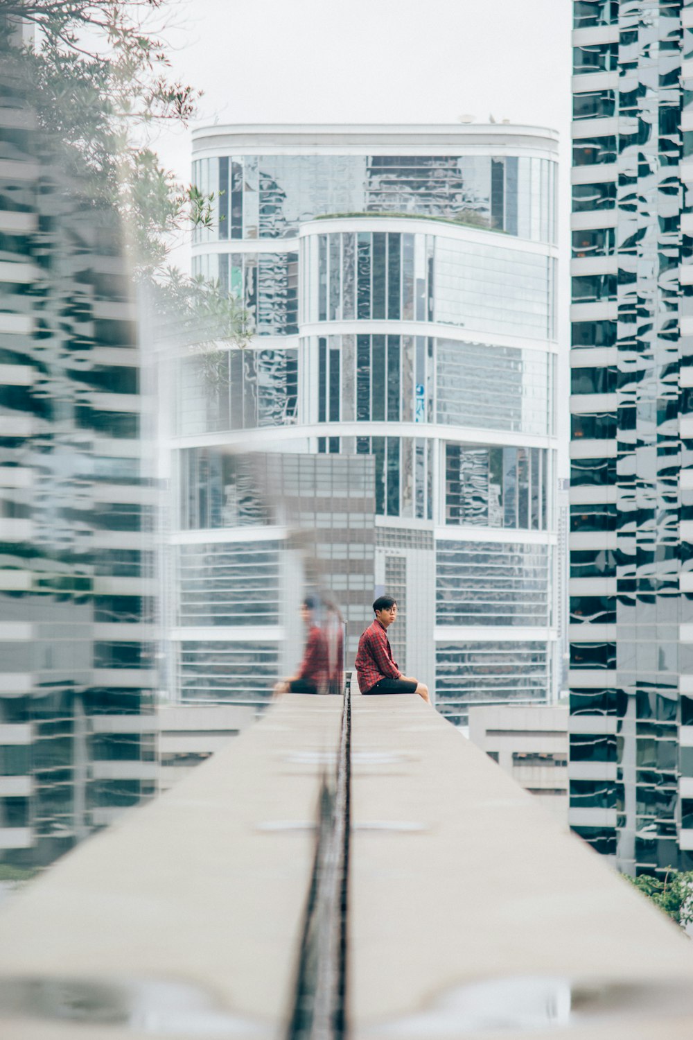 person sitting on white concrete framed near glass high rise building