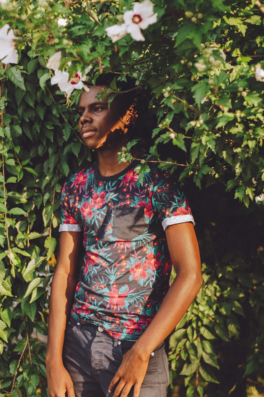 man wearing black, teal, and red floral t-shirt leaning green leaf plant with white flowers