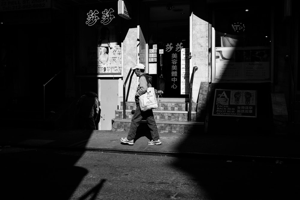 grayscale photography of person walking beside building