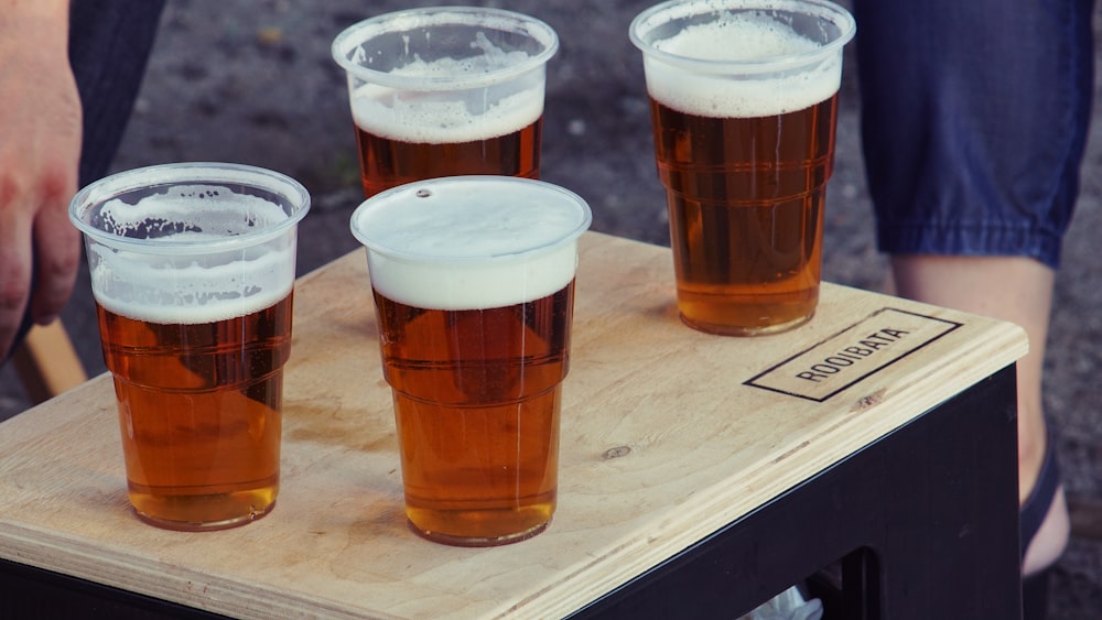 four clear plastic disposable cups with beer on the top of the board