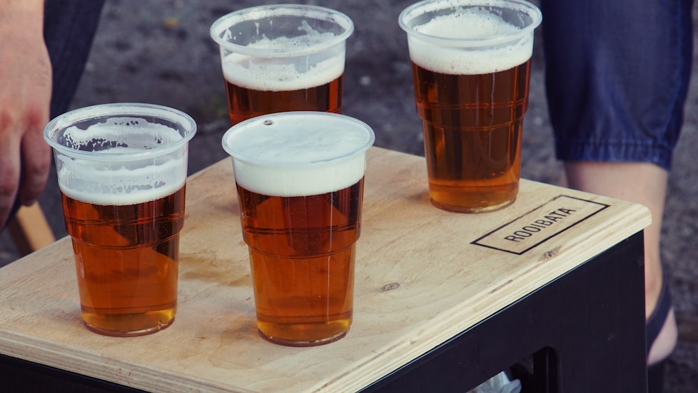 quatre gobelets jetables en plastique transparent avec de la bière sur le dessus de la planche