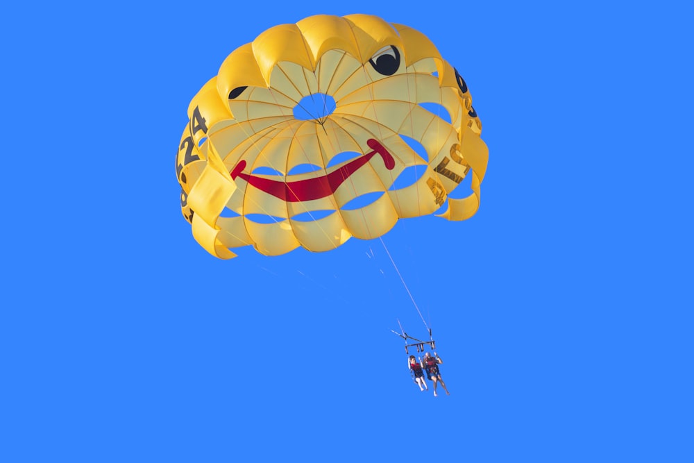 Dos personas en paracaídas amarillo, rojo y negro bajo el cielo azul durante el día