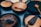An assortment of wooden kitchenware including plates, bowls, spoons, ladles, and spatulas are arranged on a flat surface. The items are made from different shades of wood, with some pieces having a polished finish while others have a more rustic appearance.