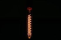 A glowing filament within a transparent Edison-style light bulb is prominently featured against a dark background. The intricate spiral design of the filament emits a warm amber light, highlighting the bulb's vintage aesthetics.