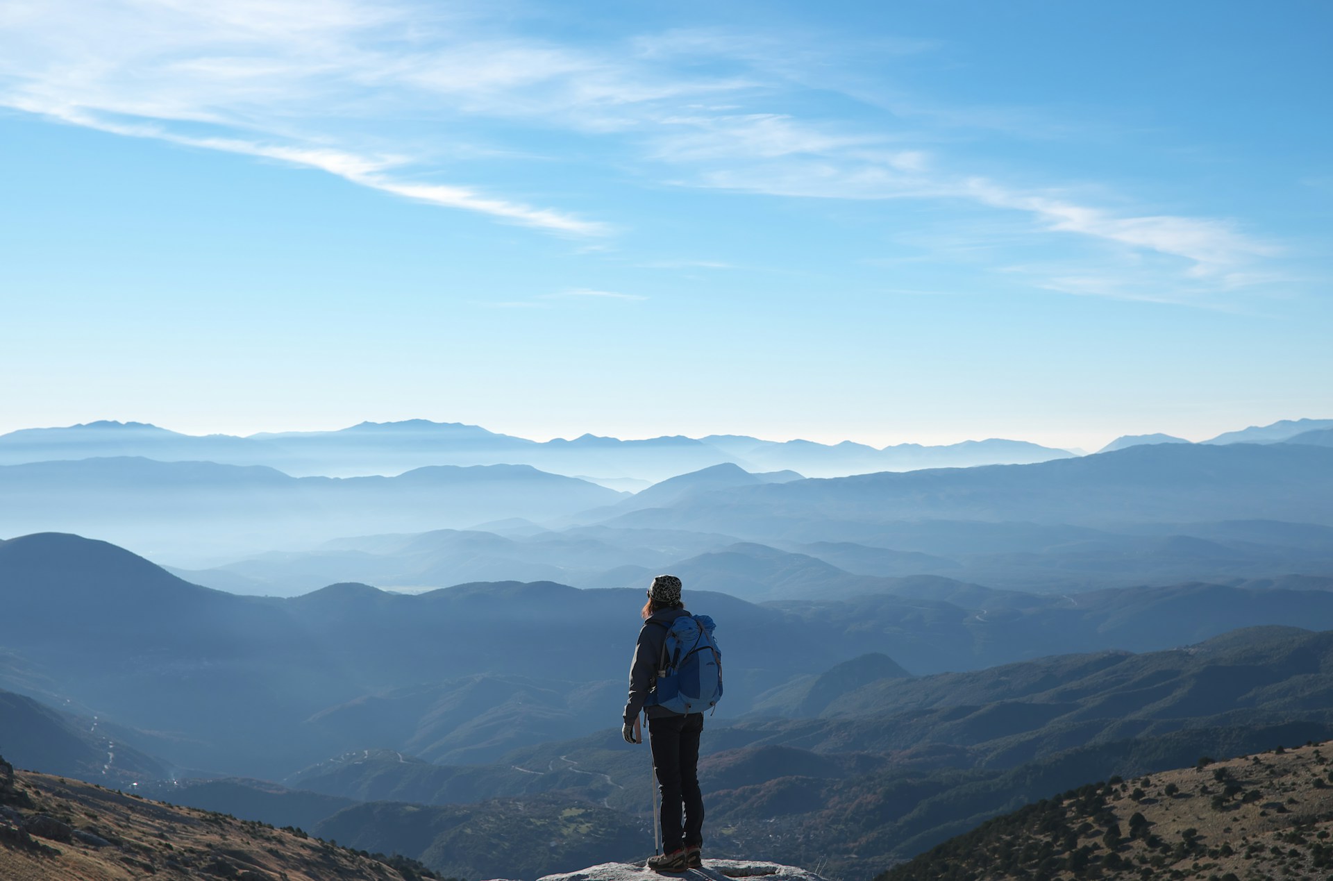 person wearing backpack standing on cliff in front of mountains during daytime