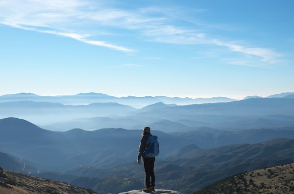 Person wearing backpack standing on cliff in front of mountains during daytime — Zagori, Greece