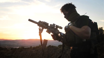 A rugged coyote hunter silhouetted against the dawn sky, holding a thermal scope-equipped rifle.