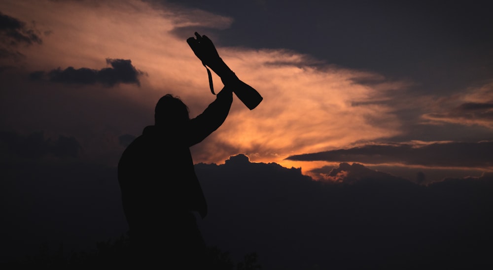 silhouette of person under cloudy skies during sunset