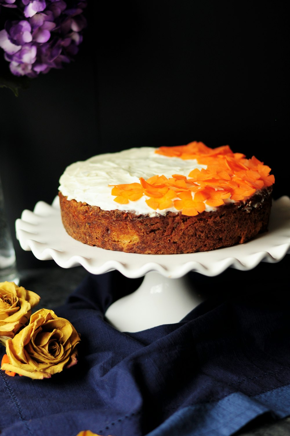 Pastel cubierto de glaseado blanco y naranja en soporte para pastel de cerámica blanca con borde festoneado