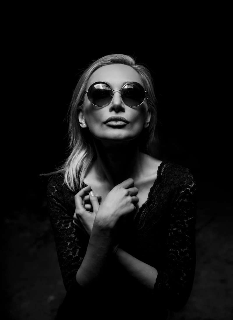 Black and white portrait of a woman in round mirrored sunglasses against a dark background