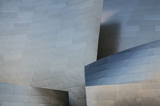 Curved and intersecting metal panels create a modern abstract architectural design. The surface reflects light subtly, showcasing a smooth and sleek texture.