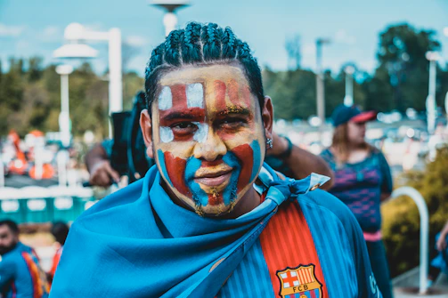 Close-up of a fan's painted face in blue and white colors cheering loudly.