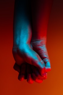 two person holding hands near orange background
