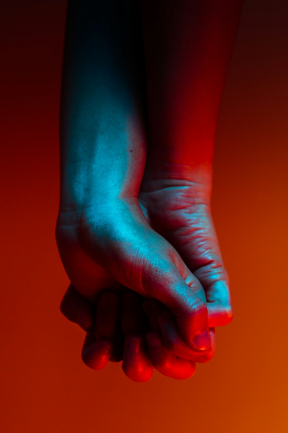two person holding hands near orange background