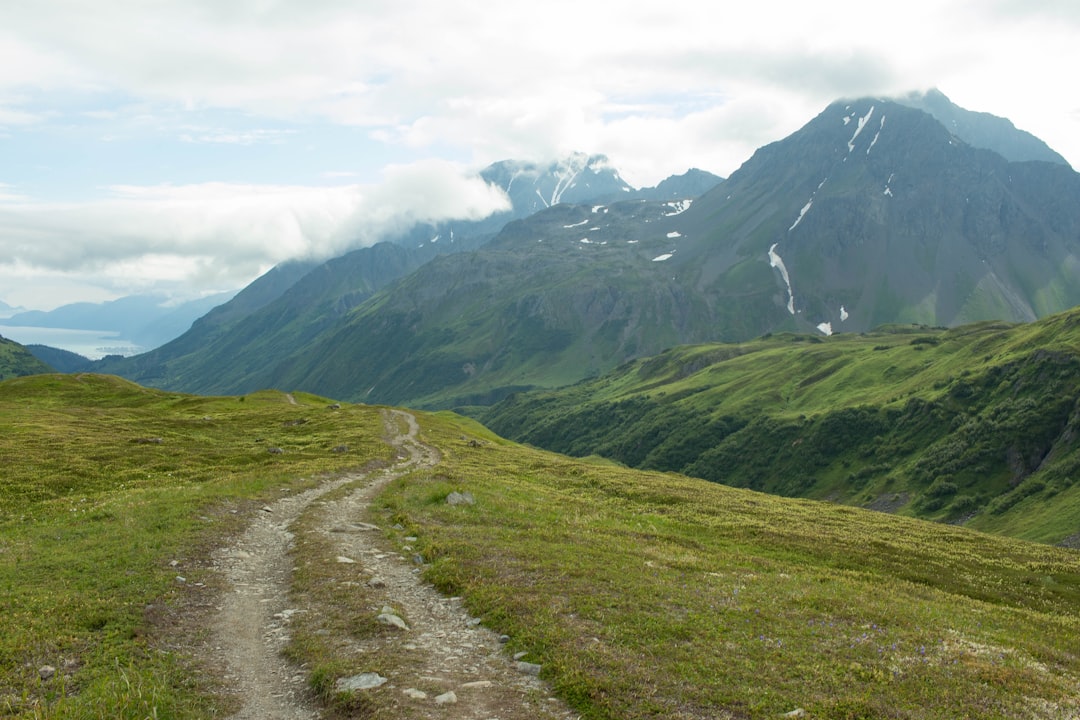 green grass field near mountain under white clouds during daytime