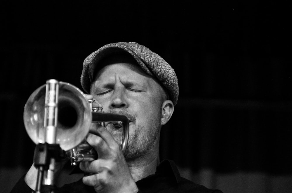 Black and white shot of man wearing flat cap wearing trumpet with eyes closed, Korpo