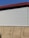 A building exterior features a combination of corrugated metal siding on the upper portion and horizontal wooden panels on the lower portion. The roof is angled and has a dark red trim. The sky is clear and blue, providing a contrasting backdrop.