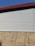 A building exterior features a combination of corrugated metal siding on the upper portion and horizontal wooden panels on the lower portion. The roof is angled and has a dark red trim. The sky is clear and blue, providing a contrasting backdrop.