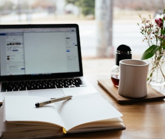 Notebook e caderno sobre a mesa junto com caneca e vaso de flor