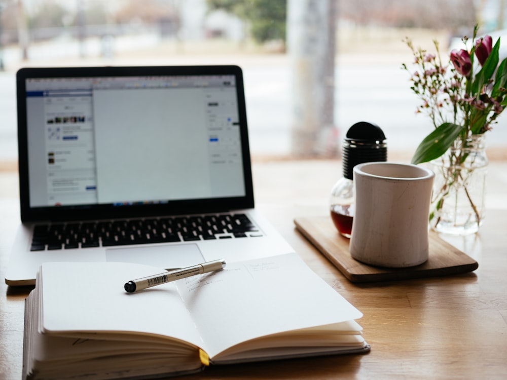 An open notebook on a wooden surface in front of a laptop