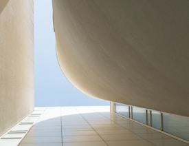 An abstract architectural scene composed of curved and angular building surfaces meeting at a V-shaped opening towards the sky, emphasizing lines, shapes, and minimalism.