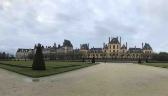 Elegant 18th-century château facade bathed in warm afternoon light, surrounded by lush greenery.