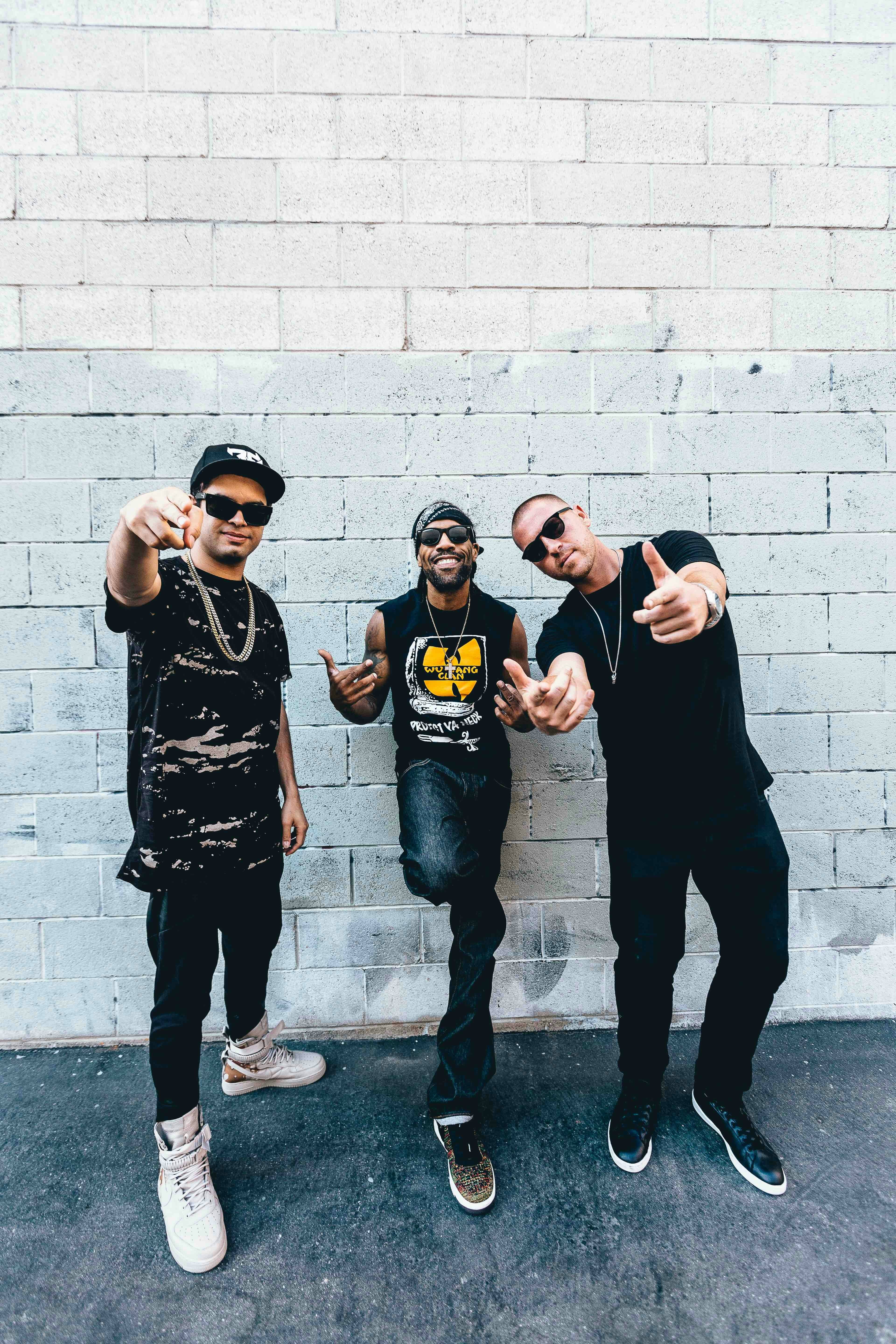 three man standing behind gray concrete wall at daytime