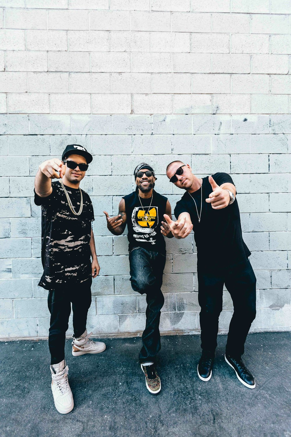 three man standing behind gray concrete wall at daytime