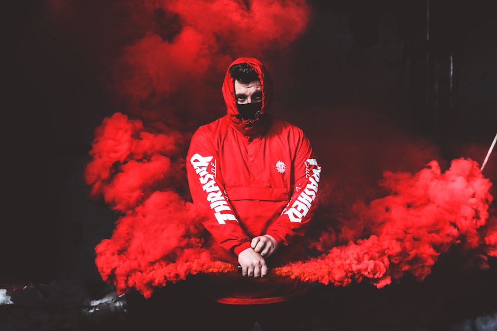 man wearing red and white hoodie and black mask surrounded by red smoke