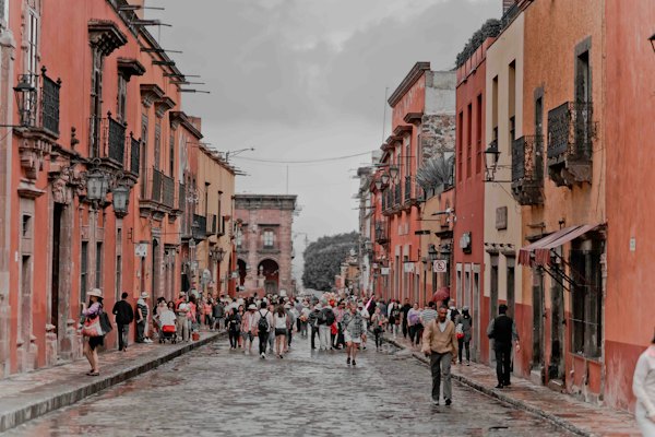 People walking between orange concrete buildings — San Miguel de Allende, Mexico