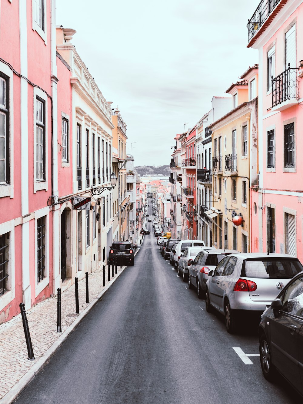 line of vehicles on the right side of a 2-way road in the middle of pink and yellow buildings during day