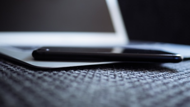 A sleek smartphone resting on a wooden desk beside a laptop and a cup of coffee, bathed in soft natural light.
