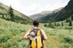 person carrying yellow and black backpack walking between green plants