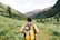 person carrying yellow and black backpack walking between green plants
