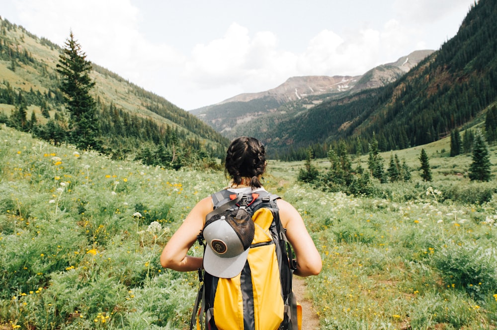 person carrying yellow and black backpack walking between green plants