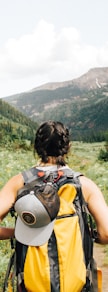 person carrying yellow and black backpack walking between green plants