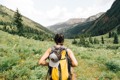 person carrying yellow and black backpack walking between green plants adventure teams background