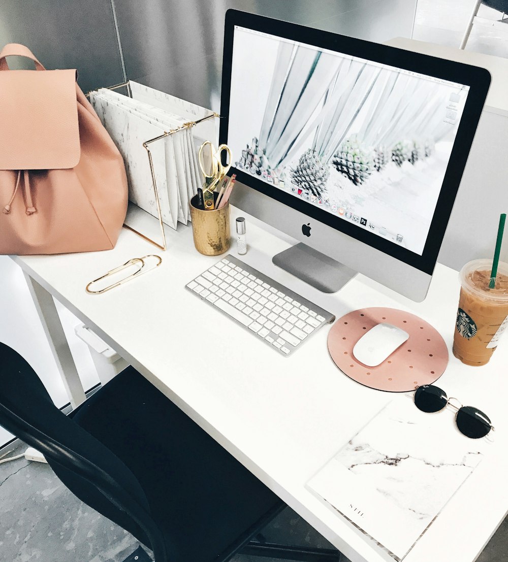 A stylish computer workspace with a leather bag and a cup of iced coffee