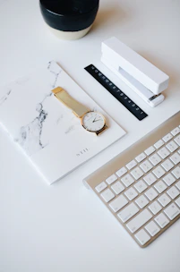 watch on top of book beside stapler near Apple keyboard