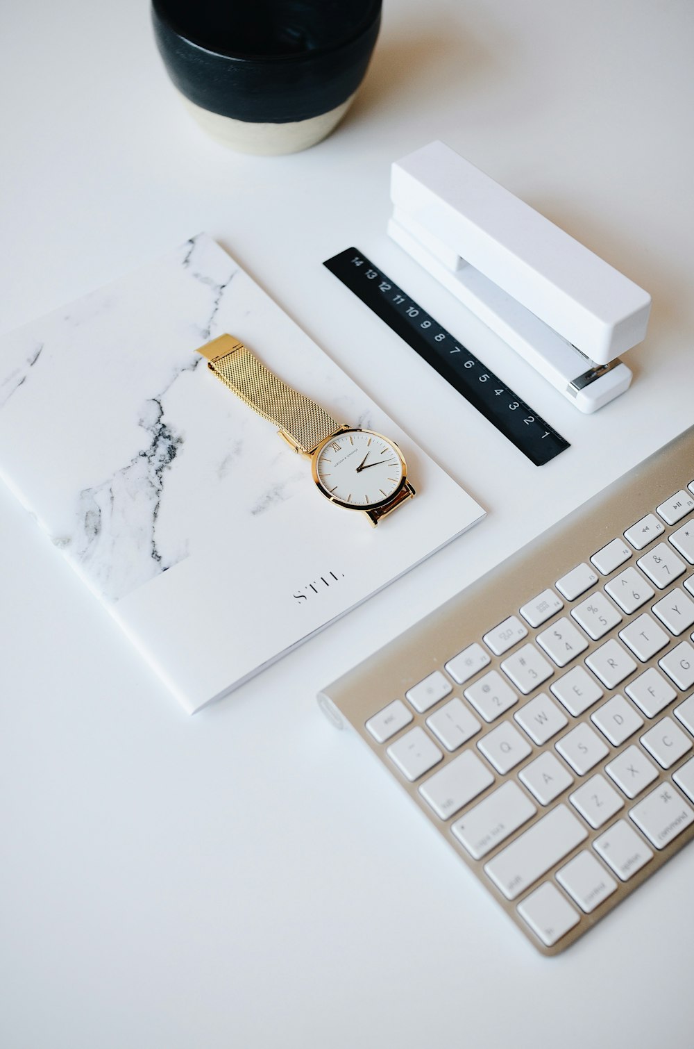 watch on top of book beside stapler near Apple keyboard