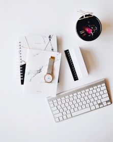 Apple Magic Keyboard near round gold-colored analog watch with silver-colored mesh band with notebook on white surface photography