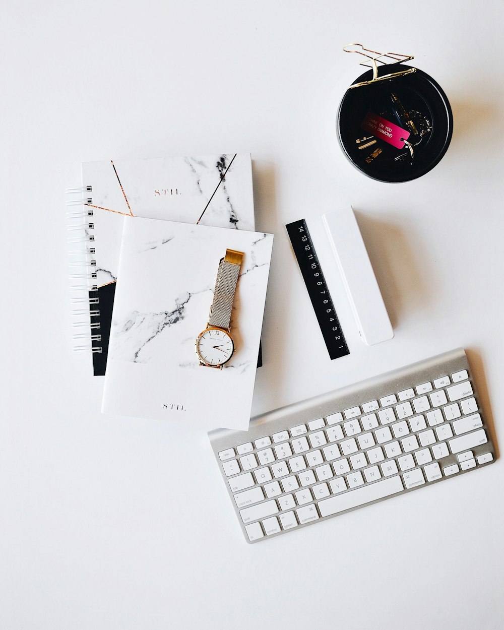 Apple Magic Keyboard near round gold-colored analog watch with silver-colored mesh band with notebook on white surface photography