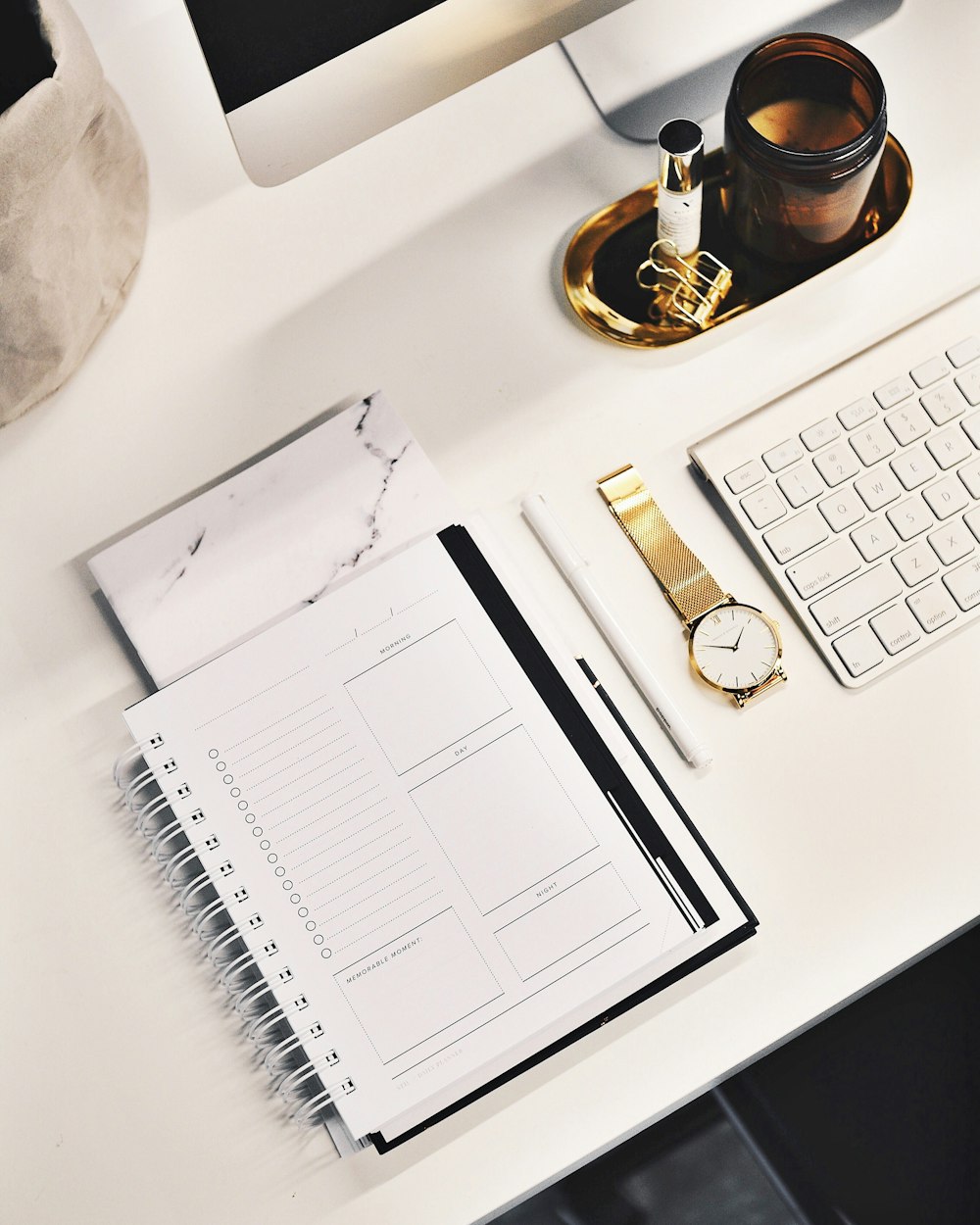A flatlay image of a desk with a keyboard, gold watch, notebook and more.