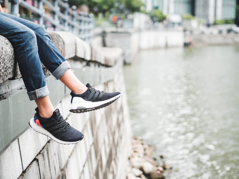 person sitting on gray ledge in front of body of water