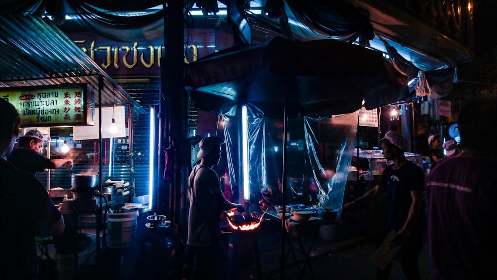 man grilling meat while man in black shirt standing in front of food stall