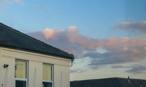 A friendly roofing expert speaking on the phone with a house in the background at sunset.