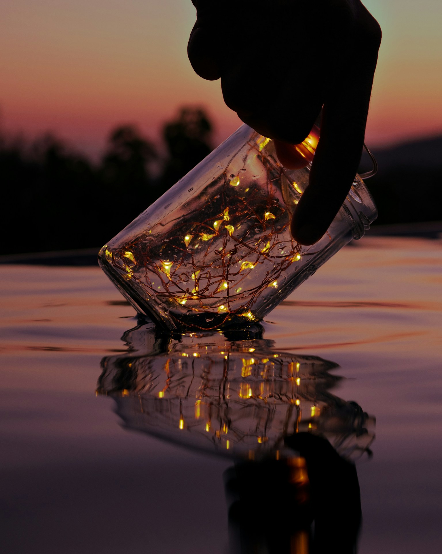 person holding string lights on clear glass jar above body of water