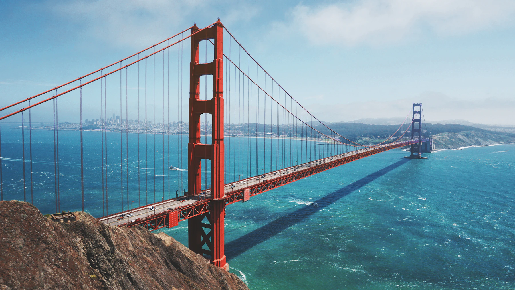 The Golden Gate Bridge crossing bright blue water beneath a clouded sky
